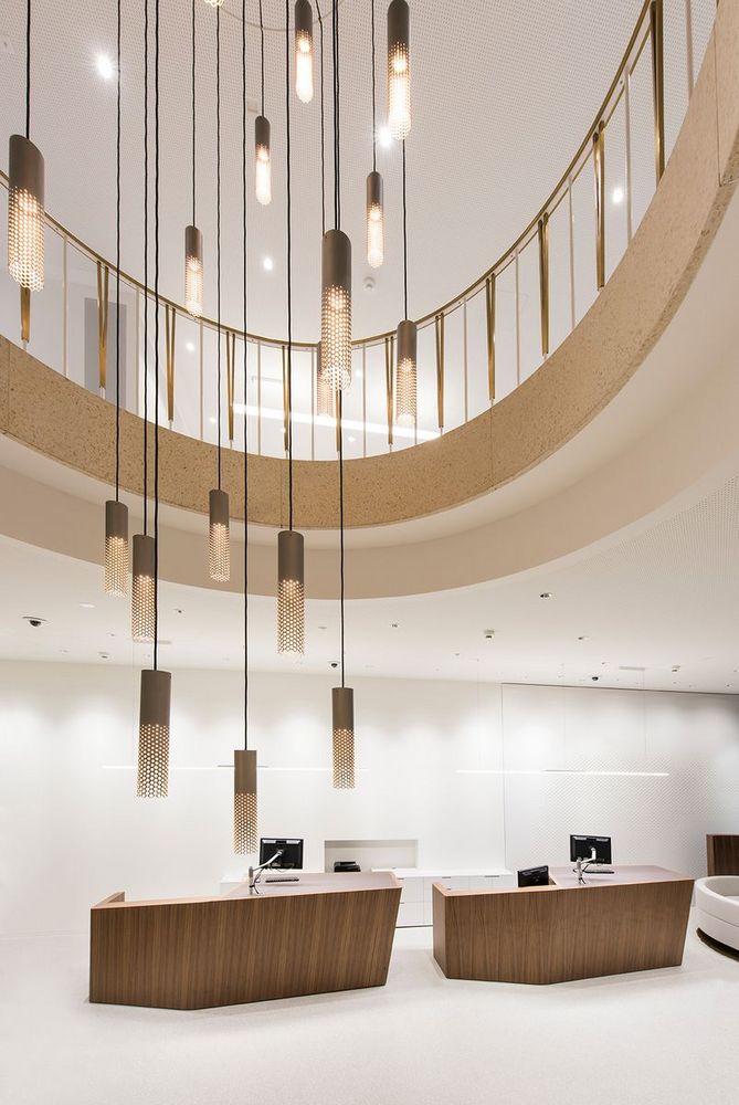 Heller Empfangsbereich der DC Bank mit modernen Holztheken und langen, hängenden Lichterelementen unter einer offenen Galerie.